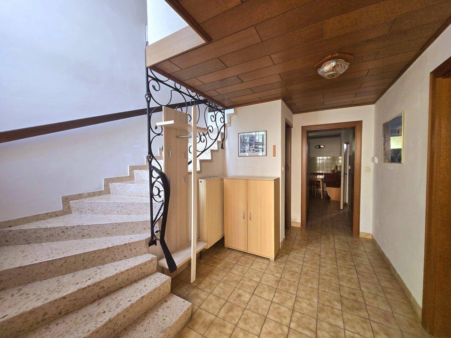 Eingangsbereich mit Steintreppe, schmiedeeisernem Geländer und Holzdecke.