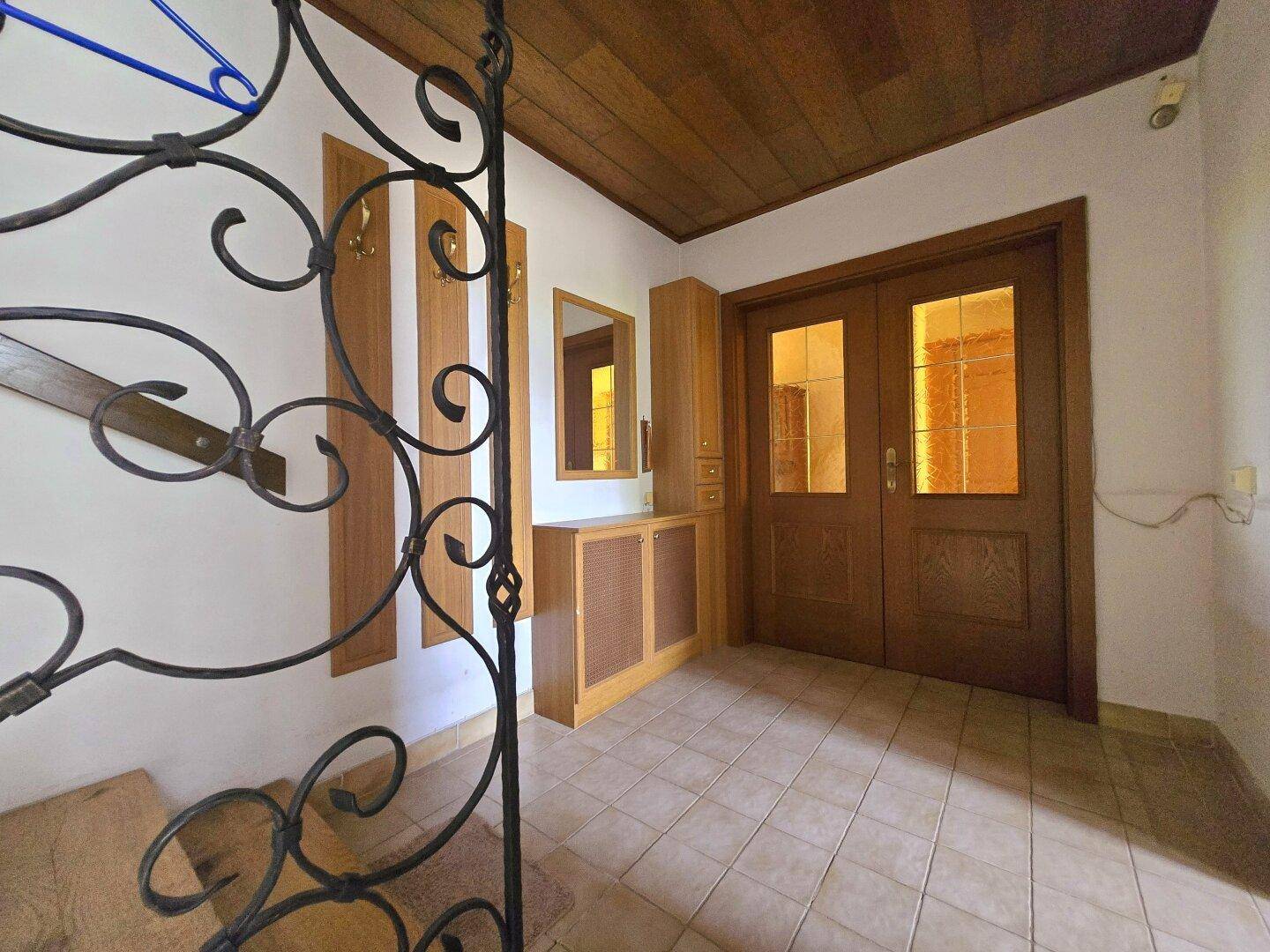 Eingangsbereich mit doppelter Holztür, Fliesenboden und einer Garderobe.