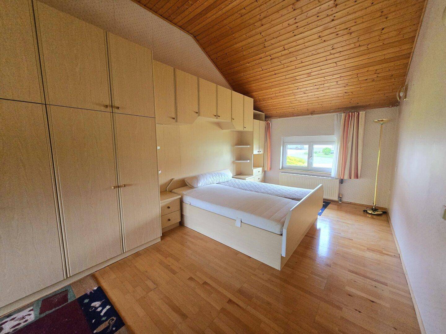Schlafzimmer mit Holzdecke, Laminatboden und Einbauschränken unter der Dachschräge.