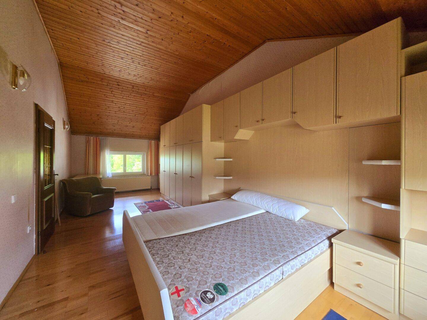 Geräumiges Schlafzimmer mit Holzdecke, Laminatboden und Einbauschränken.