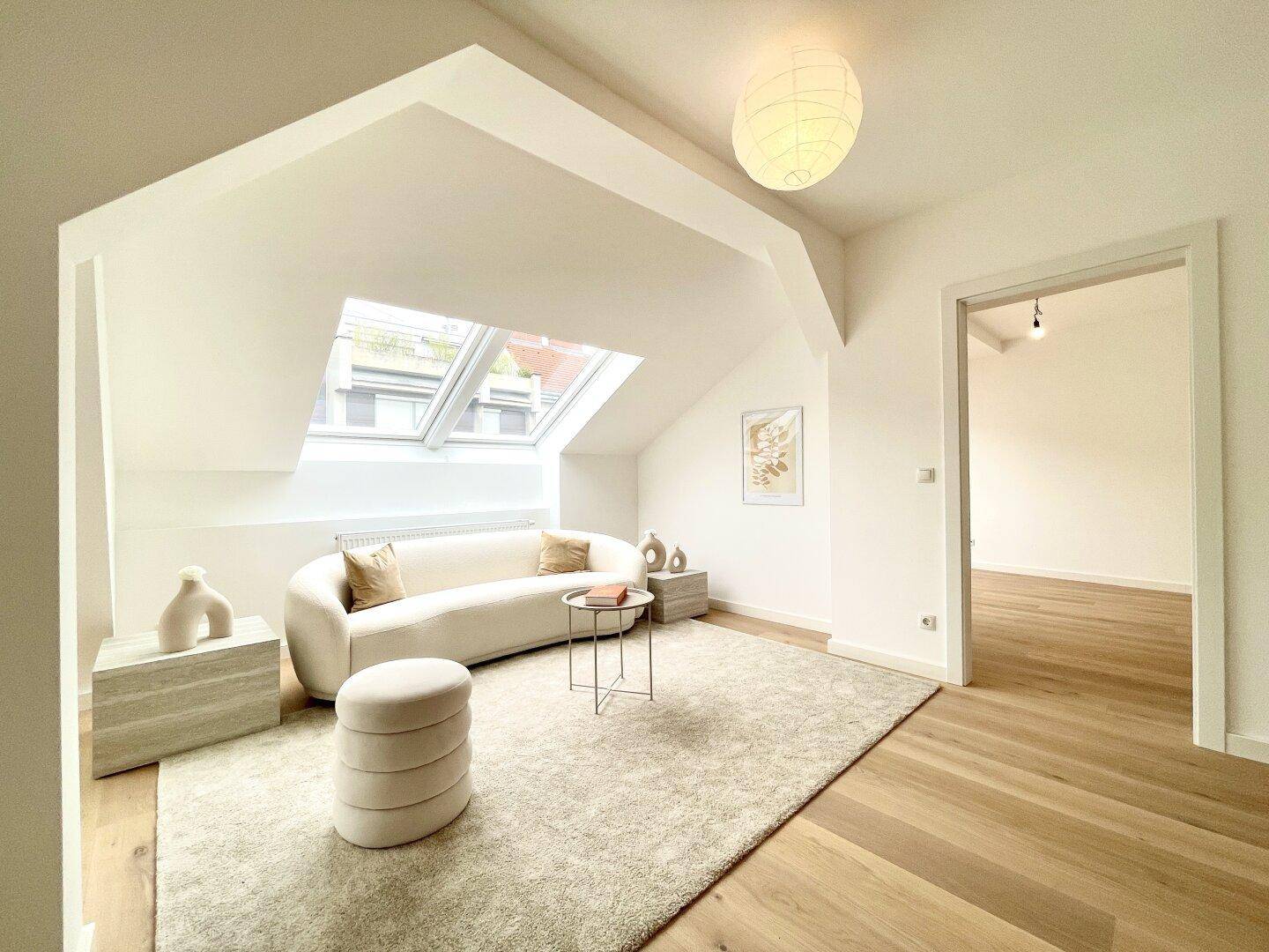 Modernes Wohnzimmer mit beigem Sofa, Teppich und viel Tageslicht durch Dachfenster.