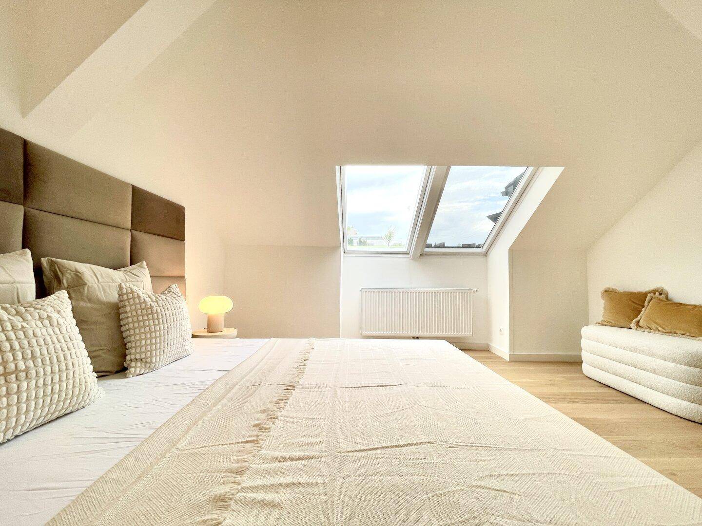 Gemütliches Schlafzimmer mit großem Bett, vielen Kissen und hellen Dachfenstern.