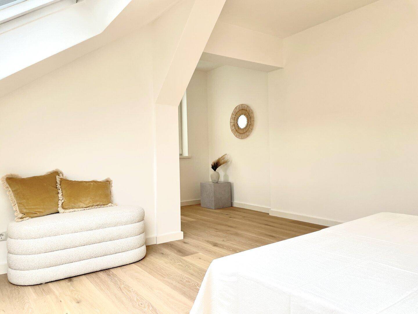 Schlafzimmer mit Holzboden, weißen Wänden und dekorativem Spiegel.