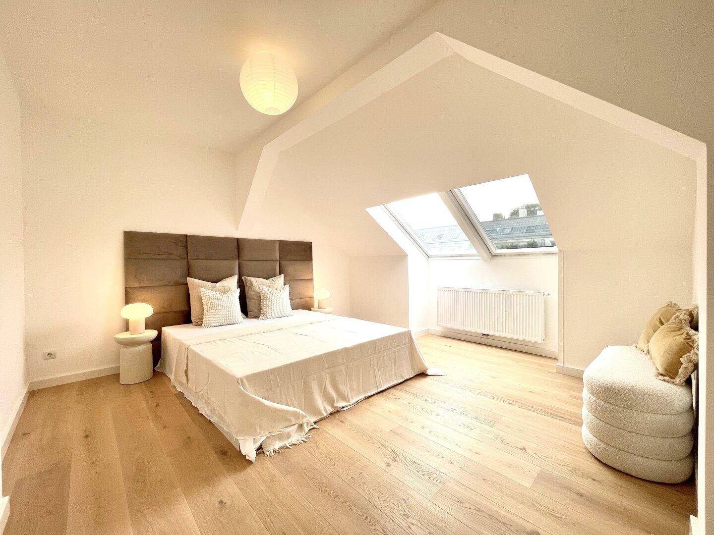 Helles Schlafzimmer mit großem Bett, gepolstertem Kopfteil und Dachfenstern.