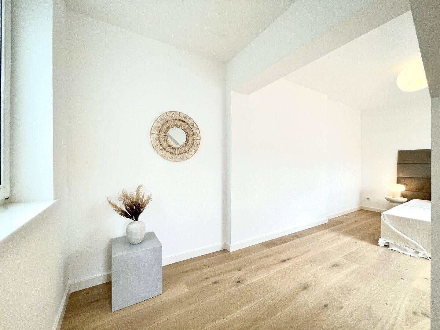 Schlafzimmer mit Holzboden, weißen Wänden und dekorativem Spiegel.