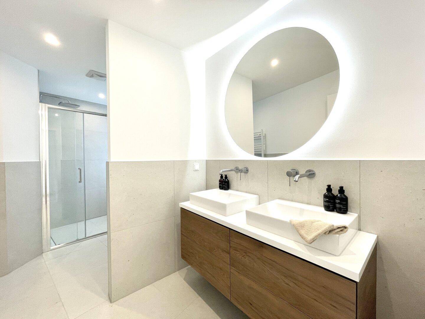 Modernes Badezimmer mit Doppelwaschbecken, beleuchtetem Spiegel und begehbarer Dusche.