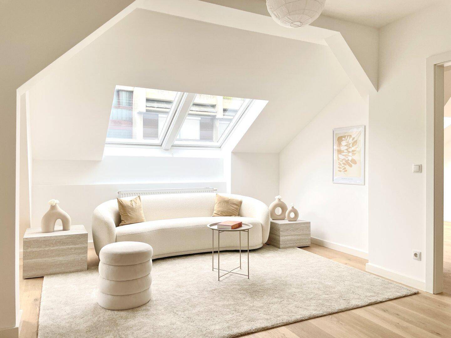 Gemütliches Wohnzimmer mit geschwungenem Sofa, Teppich und hellen Dachfenstern.