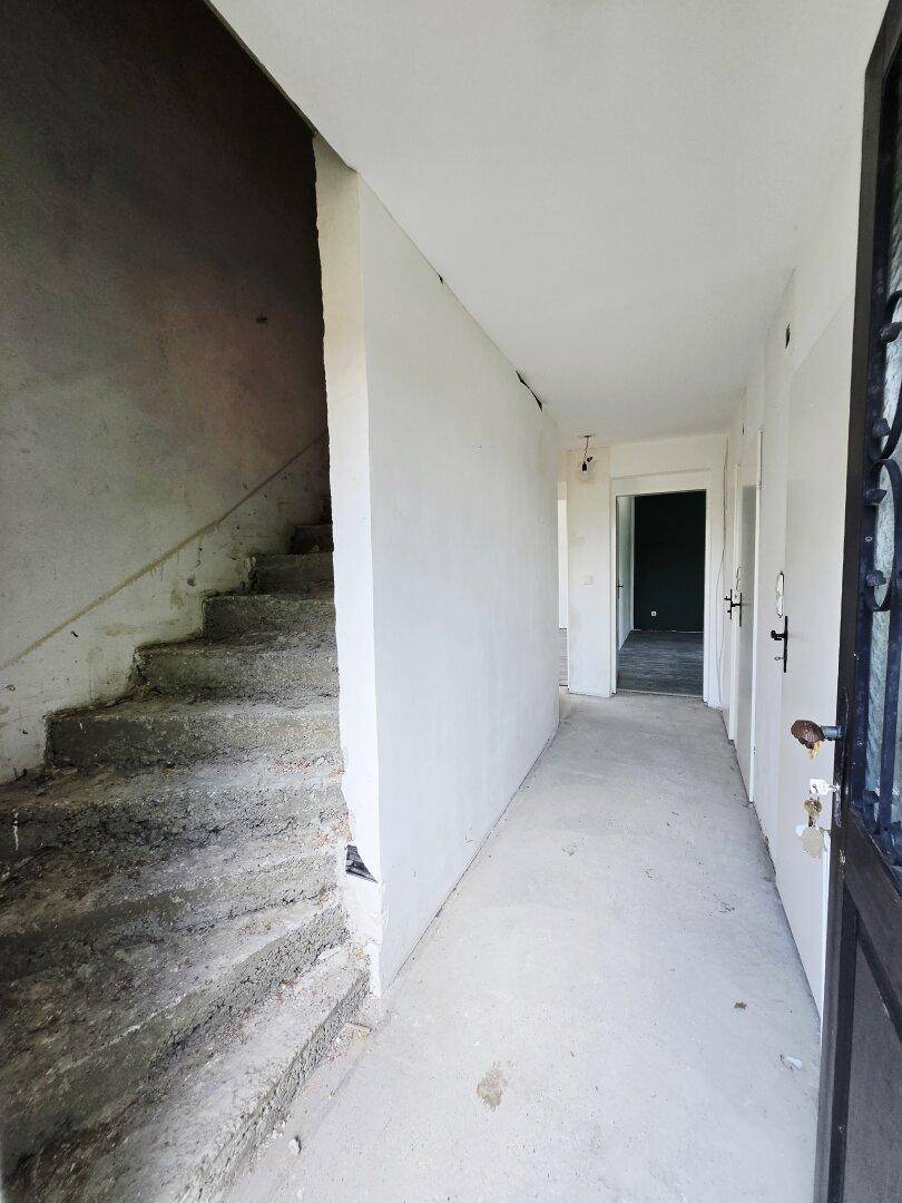 Unfertiger Flur mit Betonboden und roher Treppe, bereit für den Ausbau.
