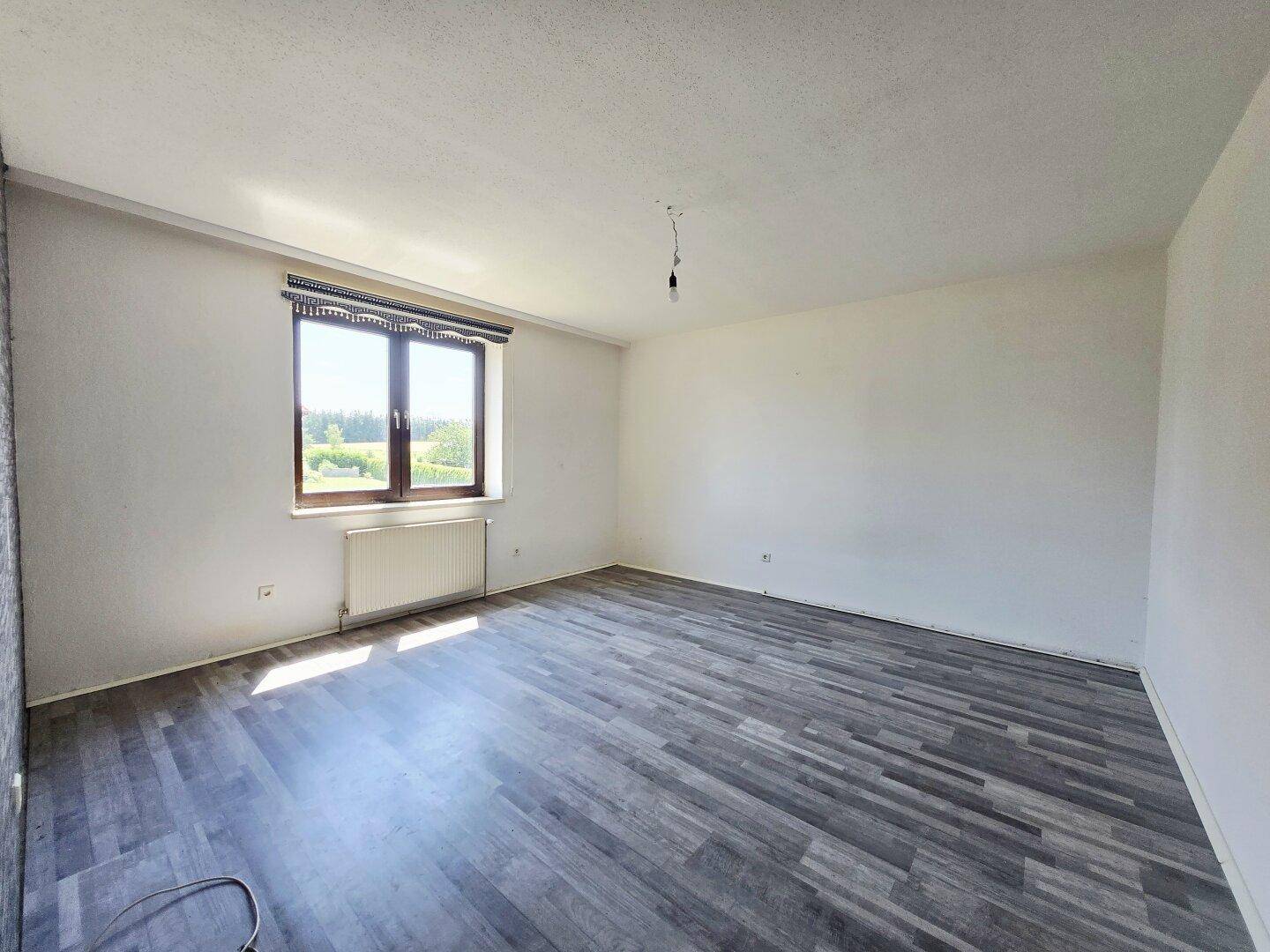 Leerer Raum mit Laminatboden und einem Fenster, das viel Tageslicht hereinlässt.