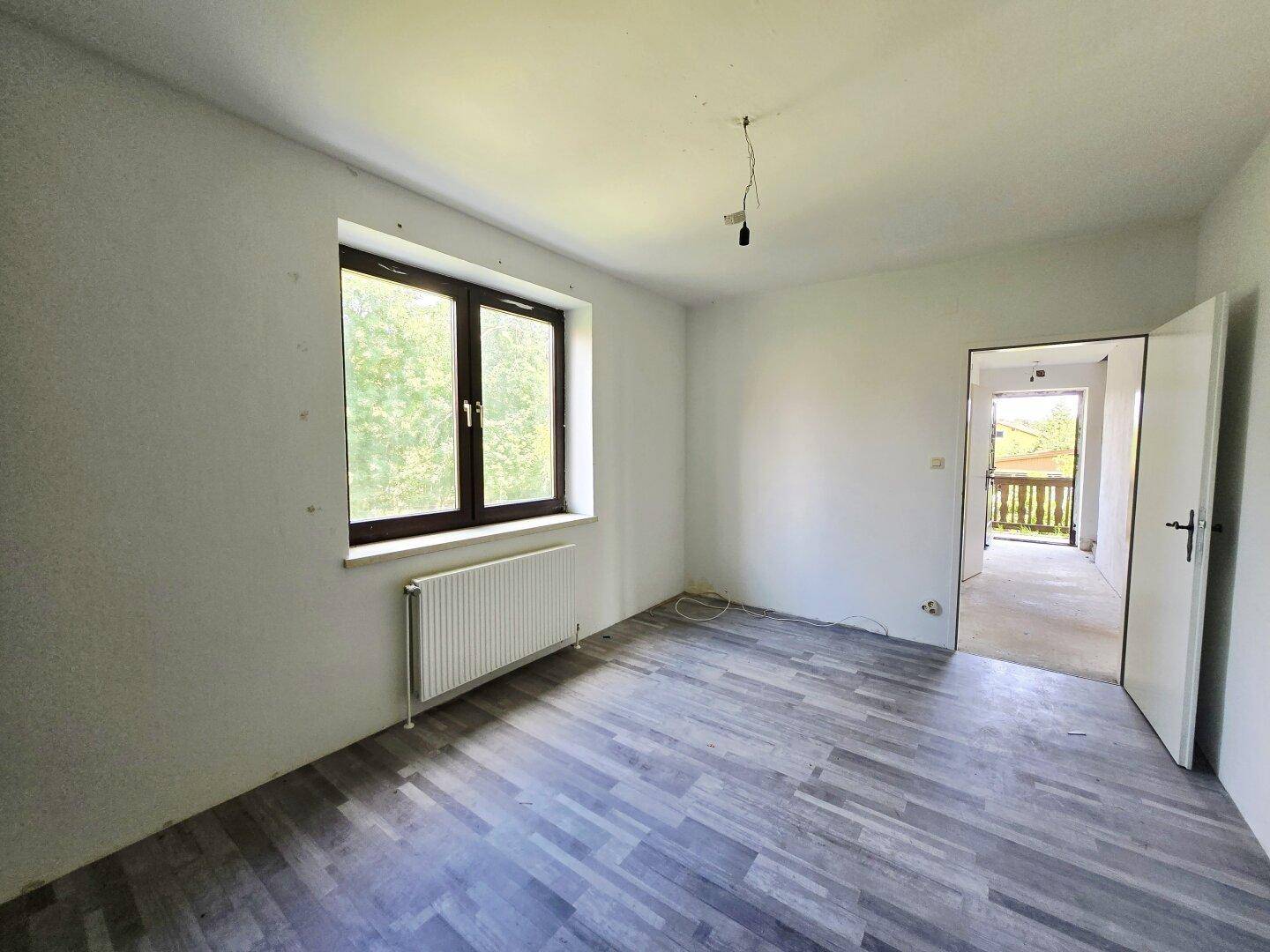 Helles Schlafzimmer mit Laminatboden und Zugang zu einem Balkon.