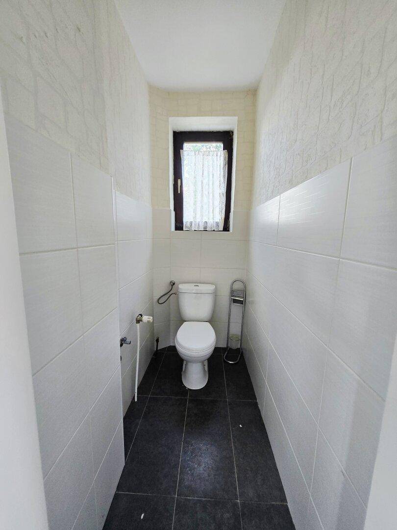 Kleines WC mit Fenster, weißen Wandfliesen und dunklem Boden.