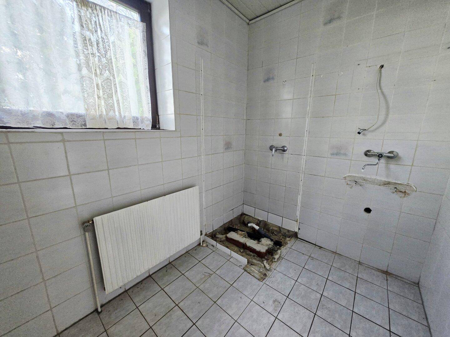 Unfertiges Badezimmer mit weißen Fliesen und Fenster, bereit für den Ausbau.