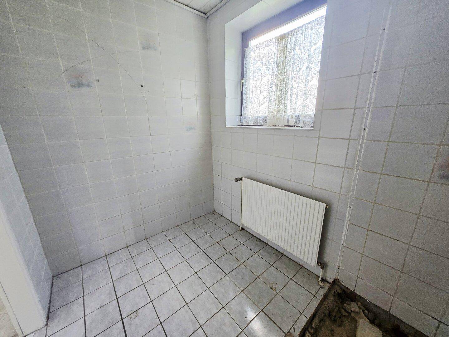 Leeres Badezimmer mit weißen Fliesen und Fenster, bereit für die Installation der Sanitärobjekte.
