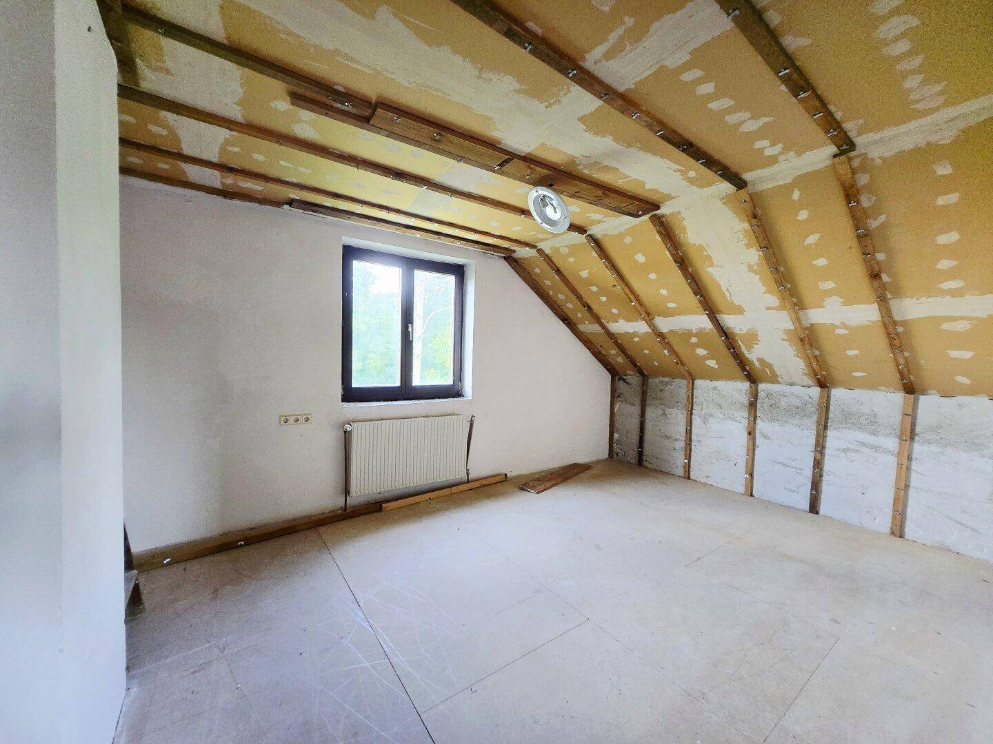 Dachbodenraum im Rohbau mit sichtbaren Holzbalken und Fenster, ideal für Ausbau.