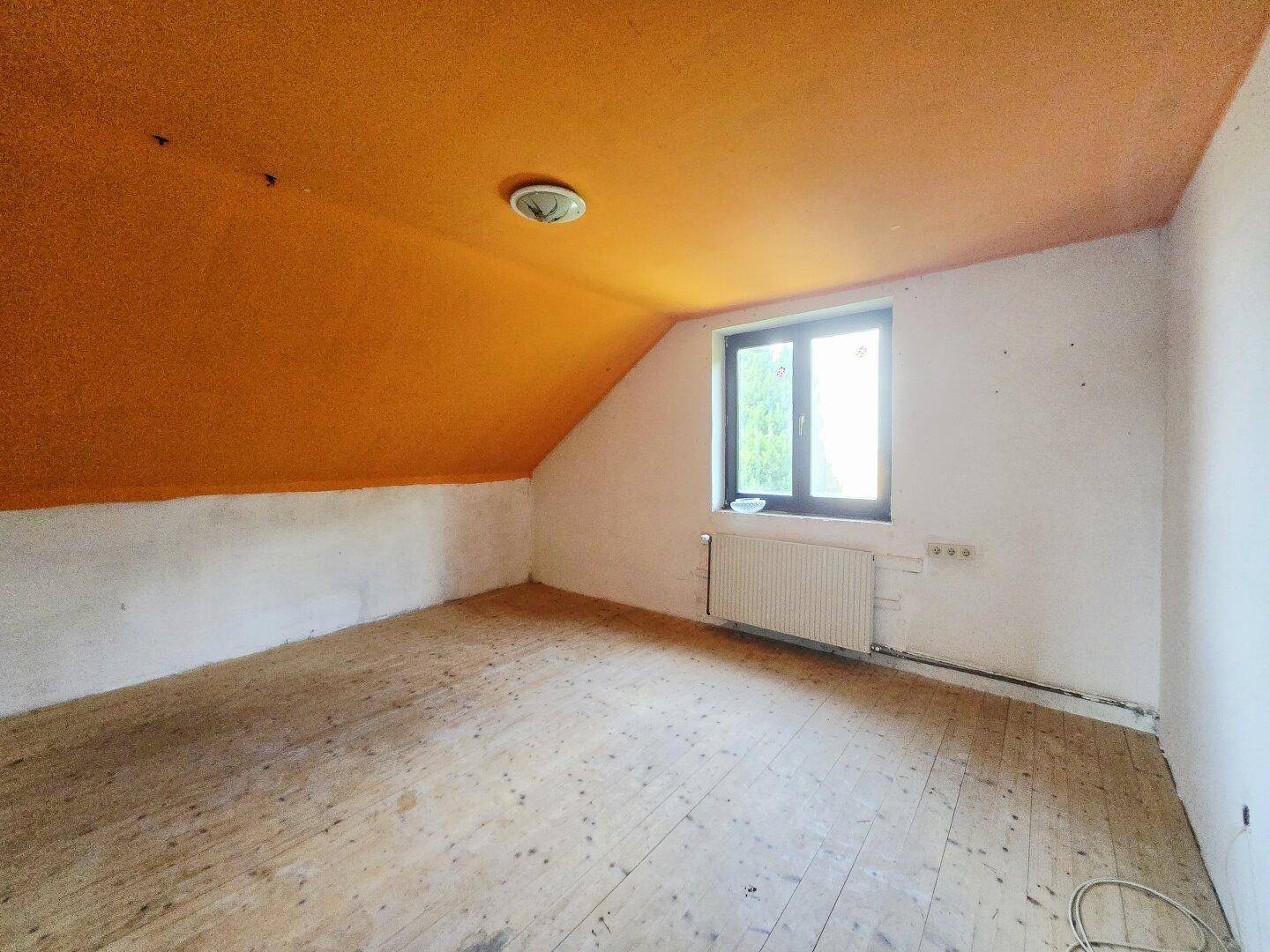 Unfertiger Dachbodenraum mit orangefarbener Decke, Holzboden und Fenster.