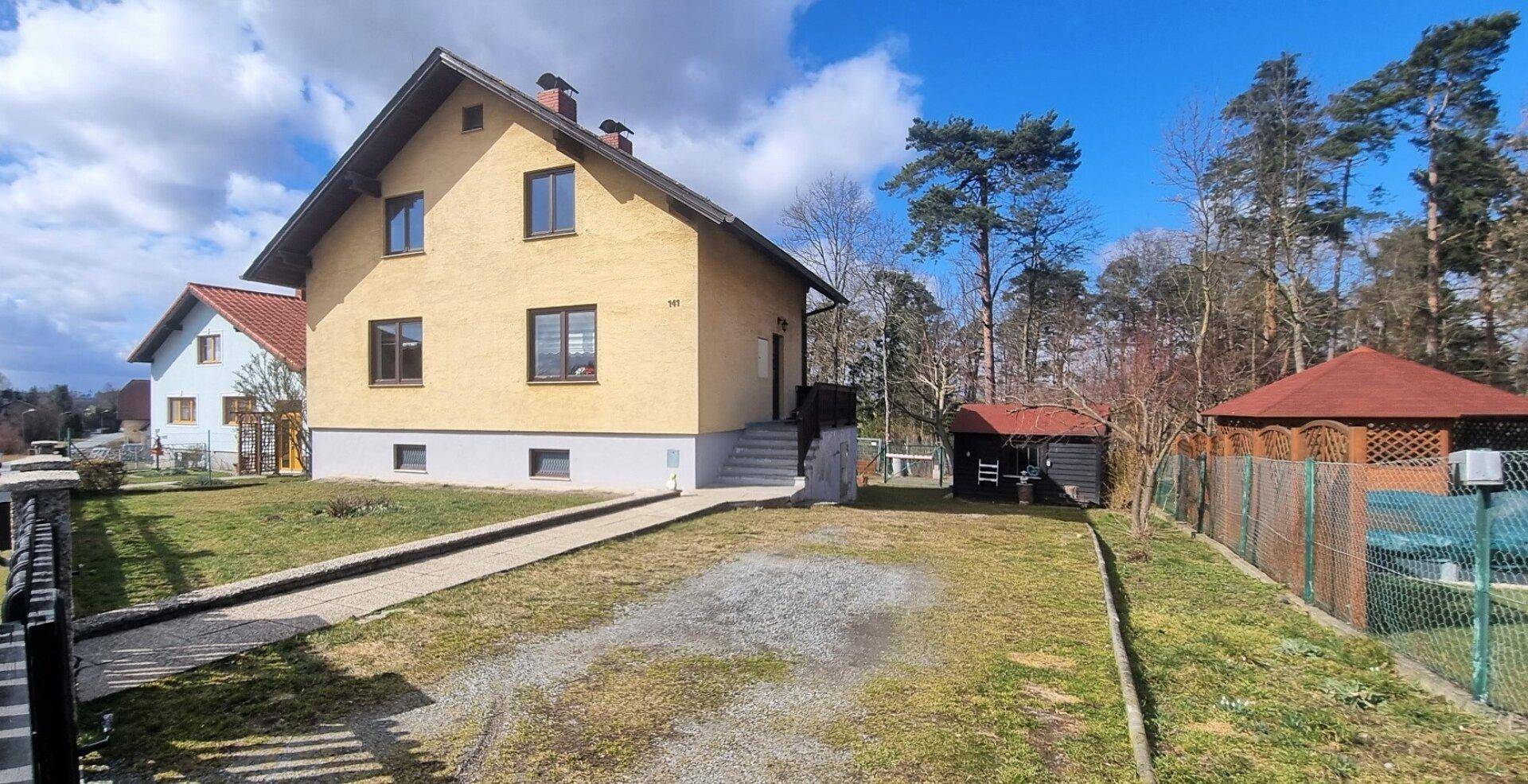 Hausfassade mit Kiesauffahrt, Garten und einem roten Pavillon im Hintergrund.