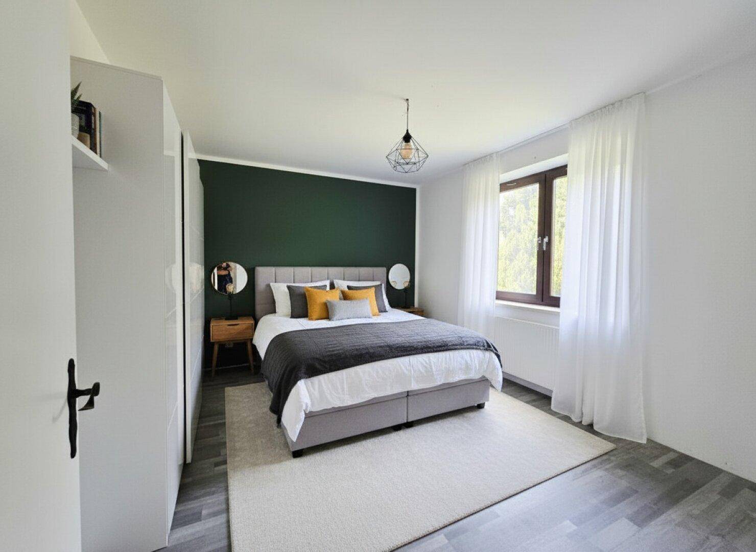 Modernes Schlafzimmer mit grün akzentuierter Wand, Doppelbett und Laminatboden.