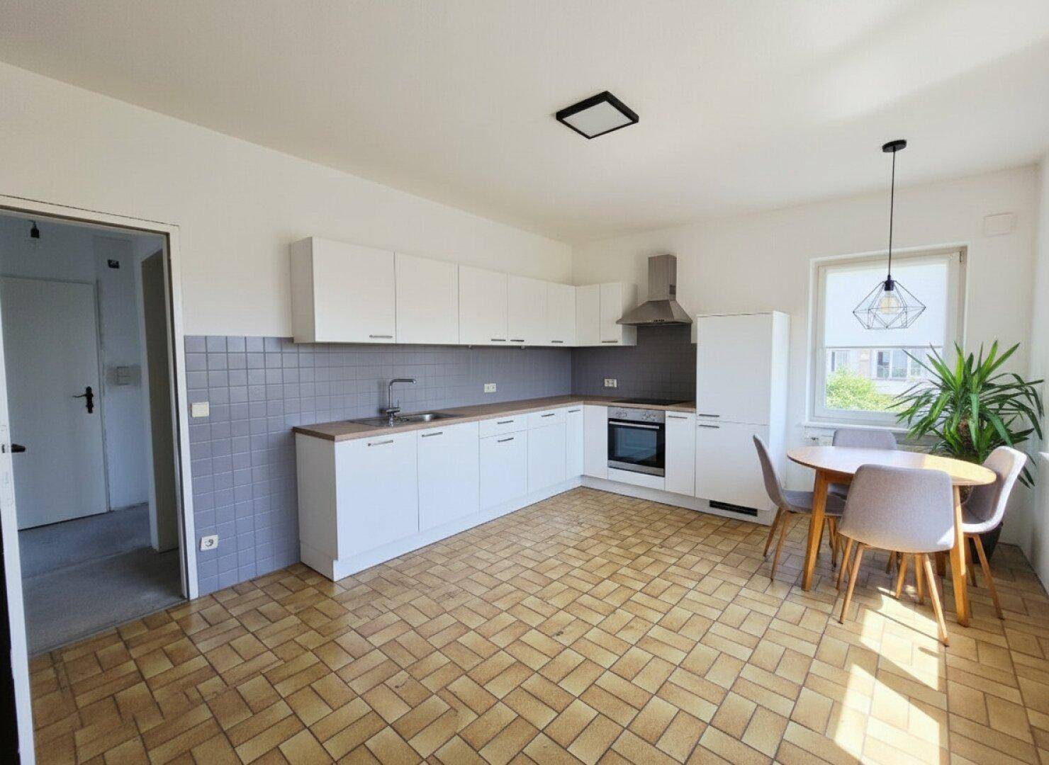 Moderne Einbauküche mit weißen Schränken, Essbereich und Fliesenboden.