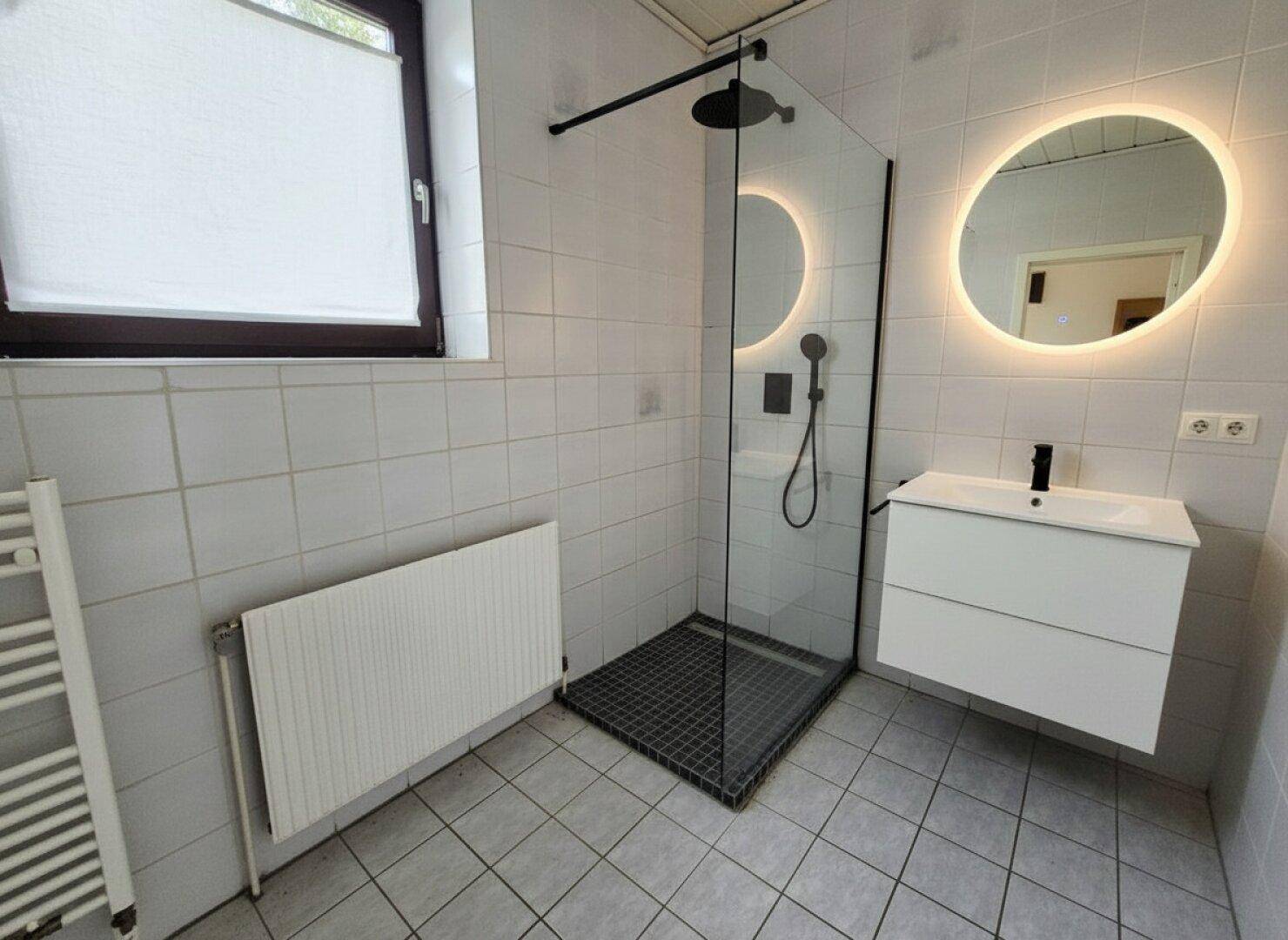Modernes Badezimmer mit ebenerdiger Dusche, beleuchtetem Spiegel und Fenster.