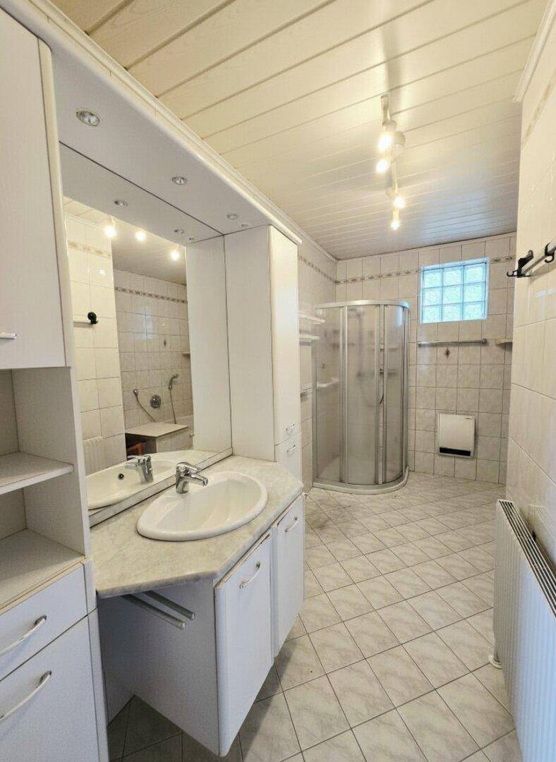 Badezimmer mit Fliesenboden, Duschkabine und einem Waschtisch mit Spiegelschrank.
