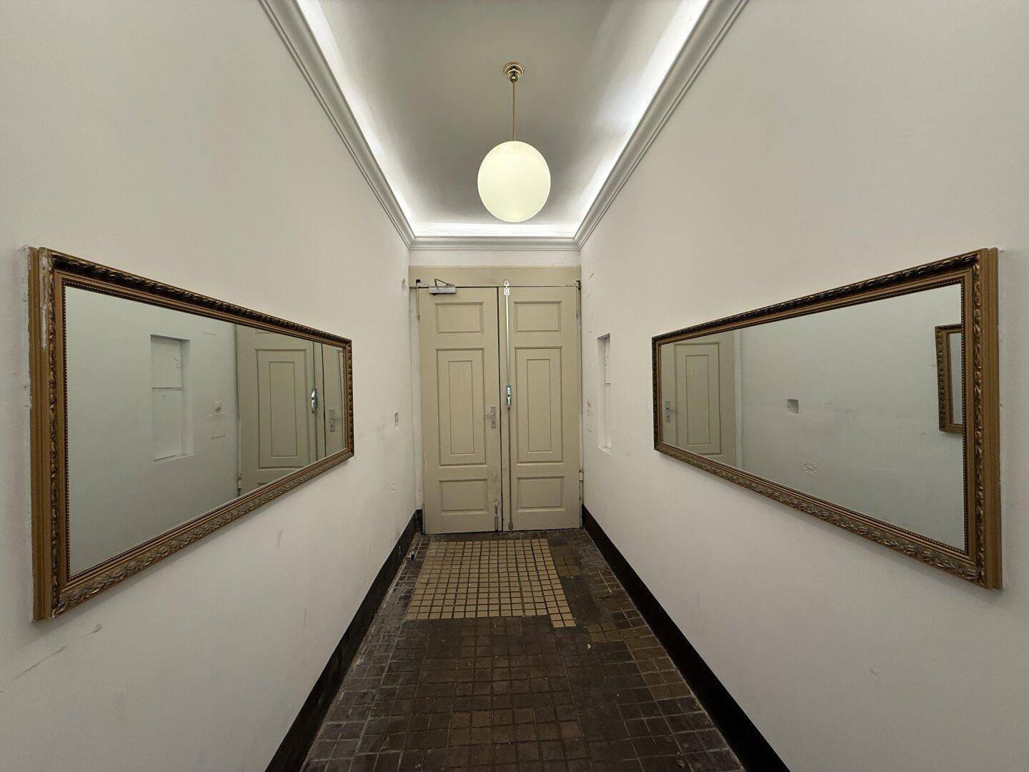 Langer Flur im Gebäude mit Spiegeln und hohen Decken, klassisch und elegant gestaltet.