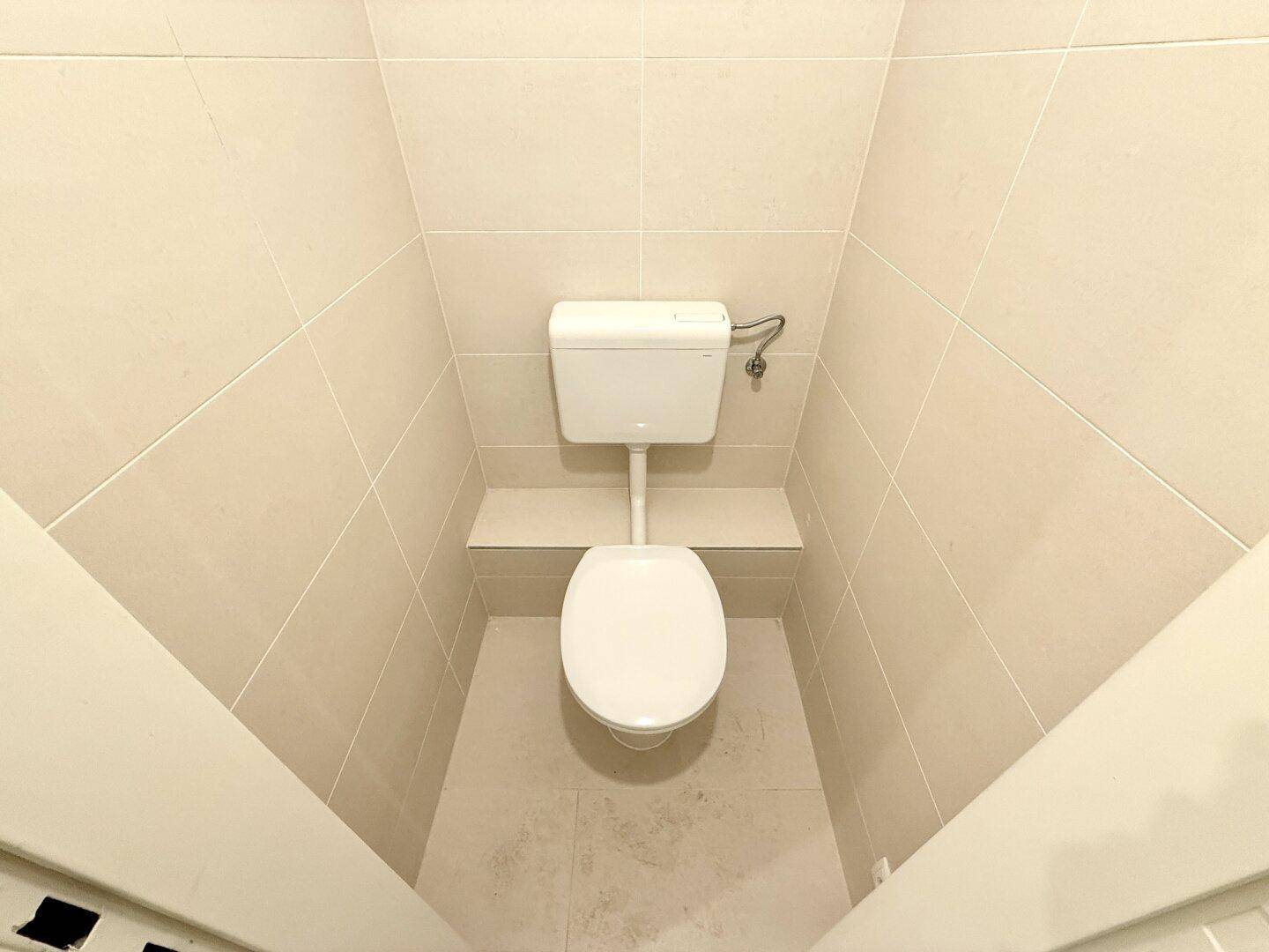 Separates WC mit hellen Fliesen und einfacher Toilette, sauber und funktional eingerichtet.