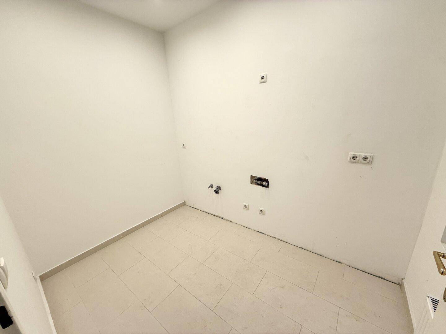 Leerer Raum mit Fliesenboden und vorbereiteten Anschlüssen, vielseitig nutzbar für verschiedene Zwecke.