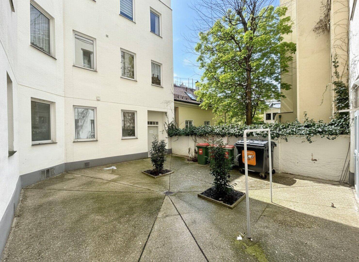 Innenhof des Gebäudes mit Bäumen und Mülltonnen, bietet einen praktischen Außenbereich.