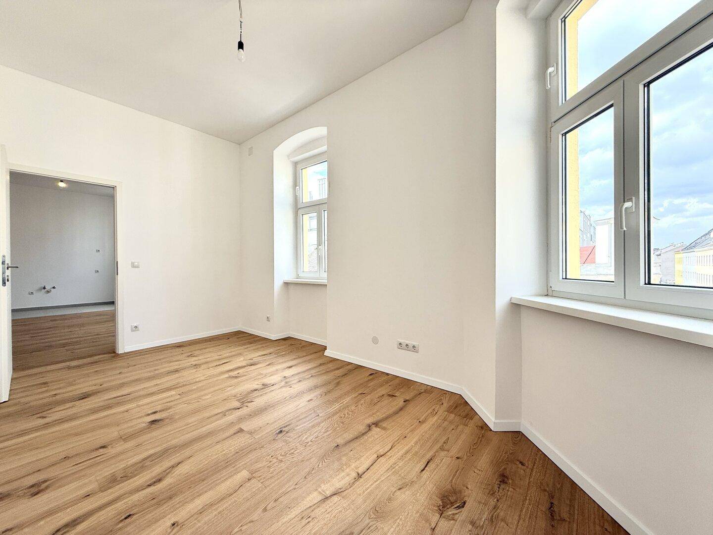 Heller Raum mit Holzboden und großen Fenstern, die einen Blick nach draußen ermöglichen.