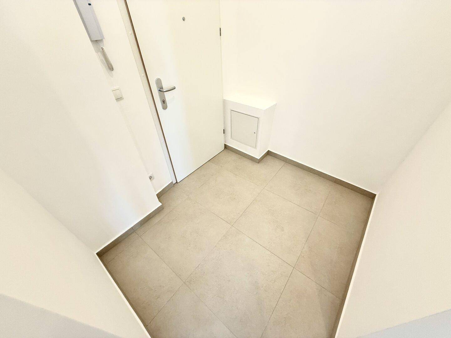 Eingangsbereich mit Fliesenboden und einer weißen Tür, die in die Wohnung führt.