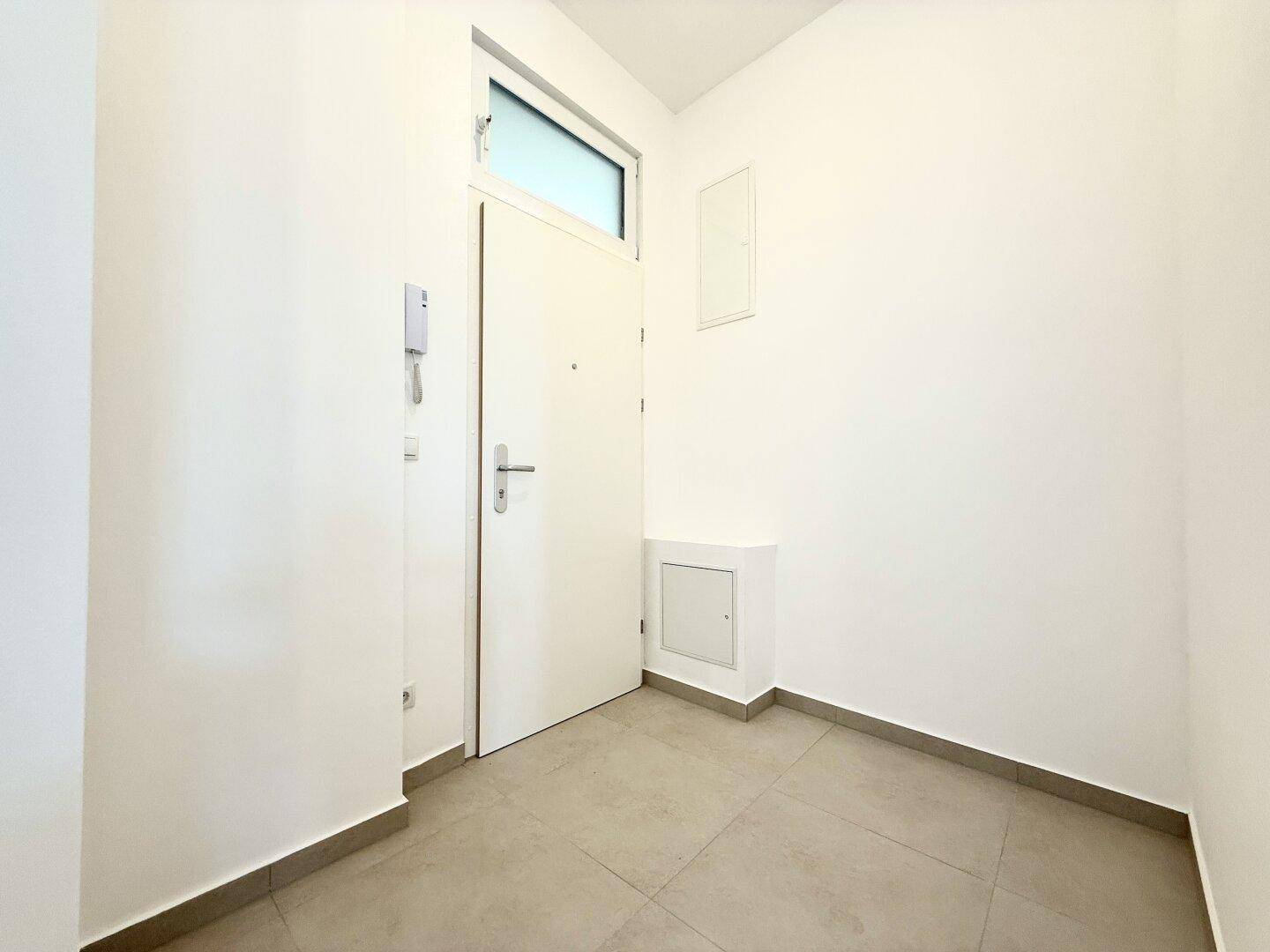 Heller Eingangsbereich mit Fliesenboden und einer modernen weißen Tür.