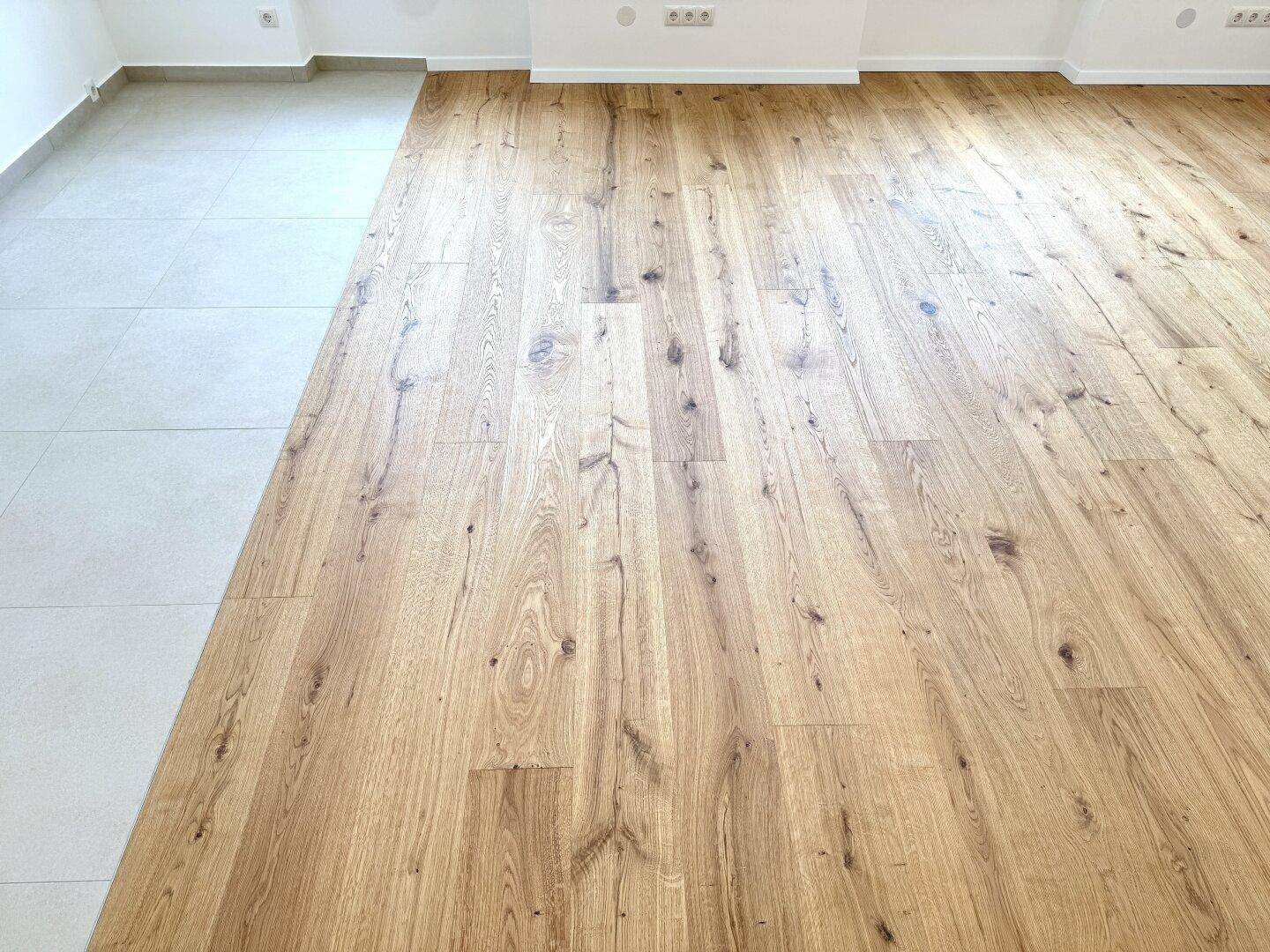 Detailaufnahme des Übergangs von hellem Fliesenboden zu warmem Holzboden.