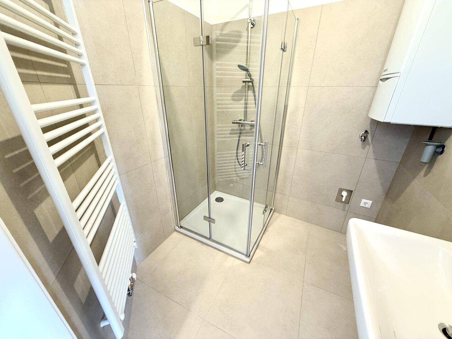 Modernes Badezimmer mit Duschkabine, Handtuchheizkörper und hellen Fliesen.