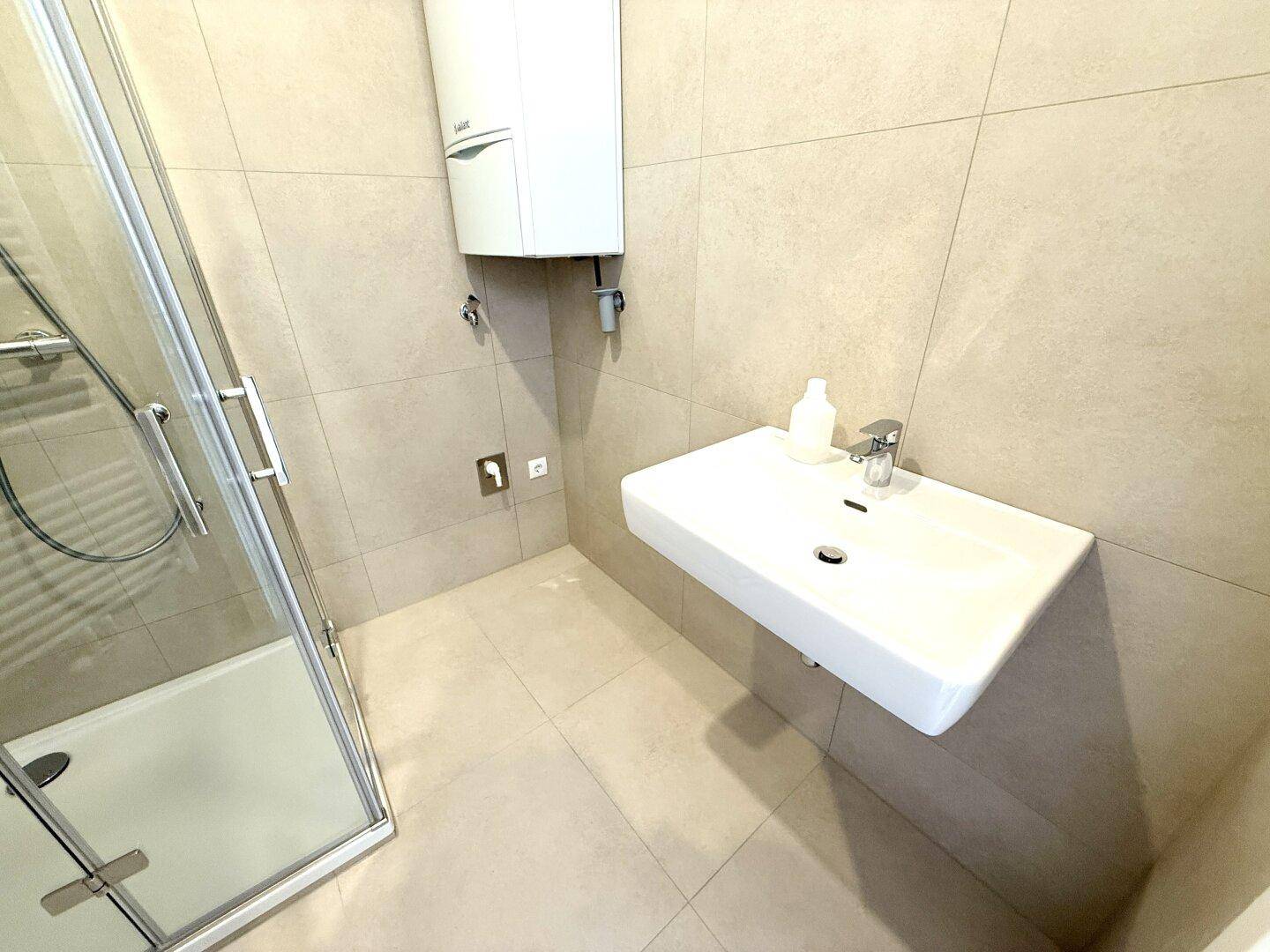 Modernes Badezimmer mit Duschkabine und einem schwebenden Waschbecken, hell gefliest.
