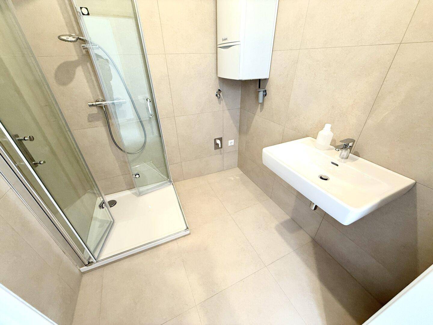 Modernes Badezimmer mit Duschkabine und einem schwebenden Waschbecken, hell gefliest.