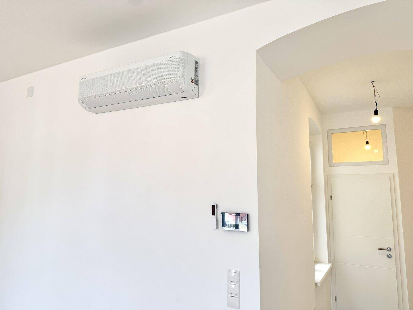 Weiße Wand mit installierter Klimaanlage und einem modernen Türrahmen.