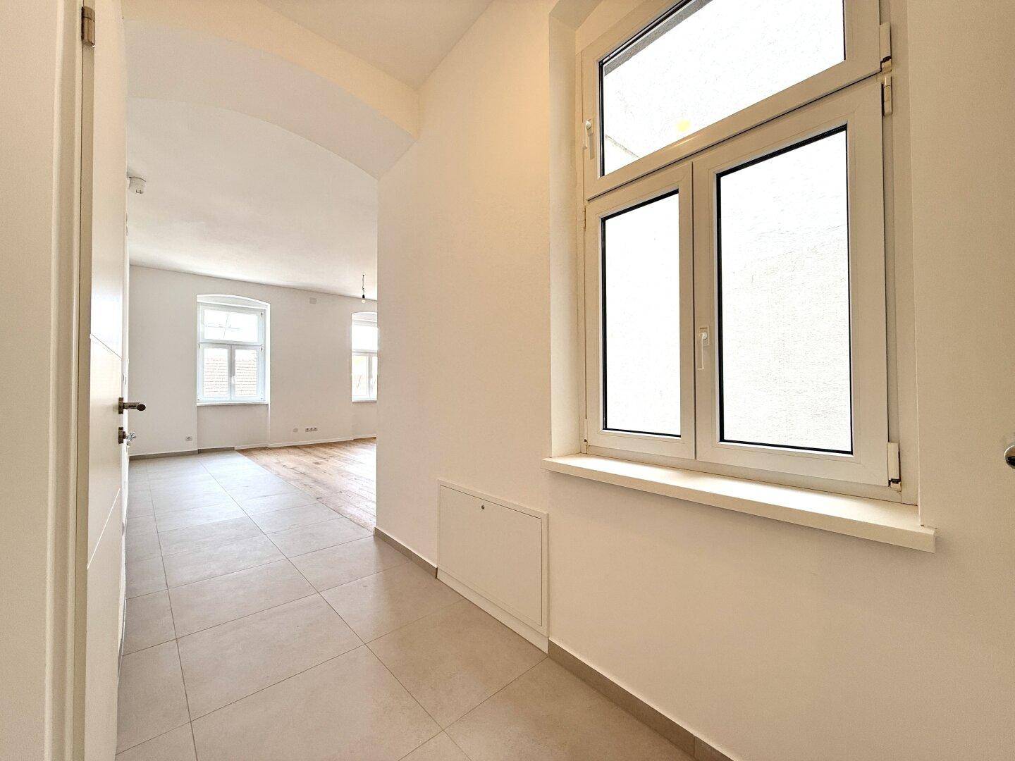 Langer Flur mit Fliesenboden und einem Fenster, das den Blick in den Wohnbereich freigibt.