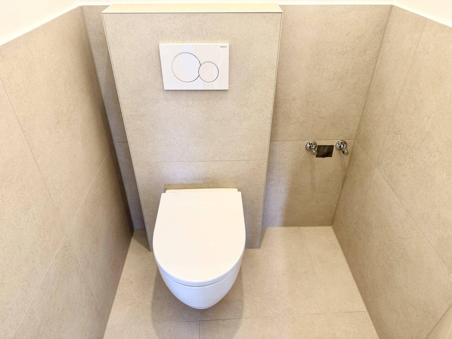 Modernes WC mit wandhängender Toilette und hellen Fliesen, minimalistisch gestaltet.