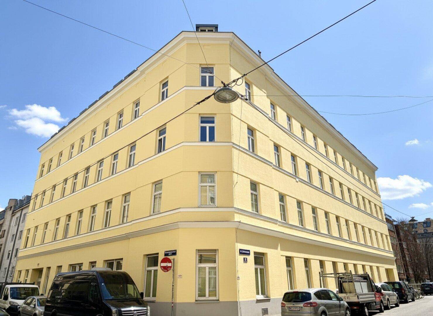 Eckgebäude mit gelber Fassade und vielen Fenstern, typisch für städtische Architektur.