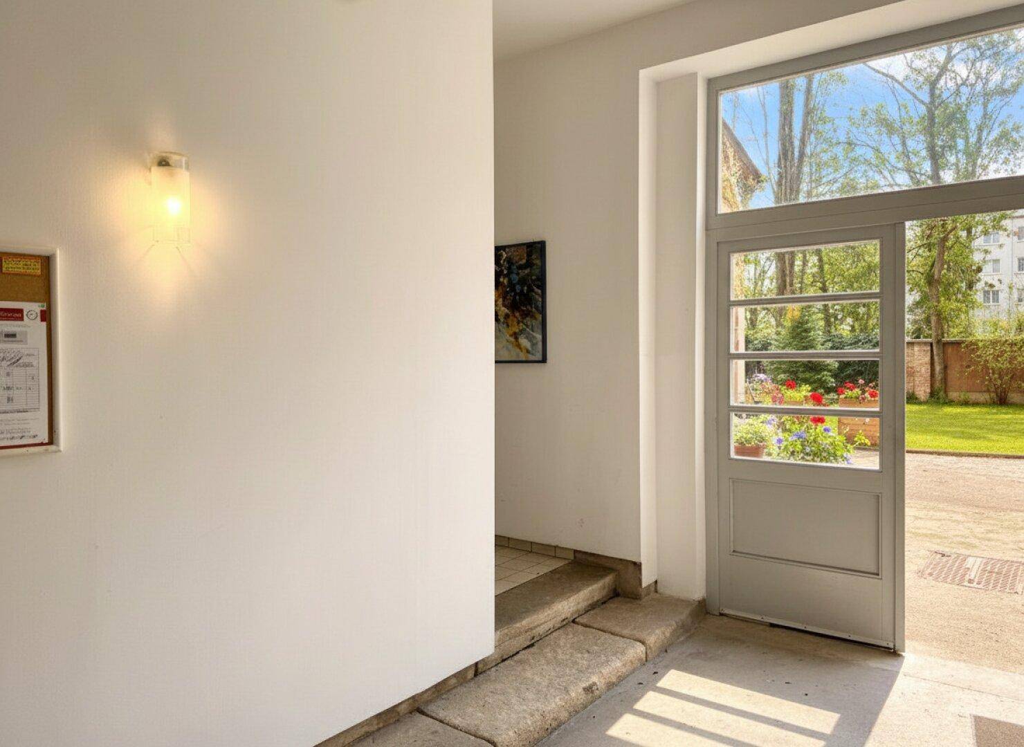 Eingangsbereich mit Glastür, die den Blick in den grünen Garten freigibt.
