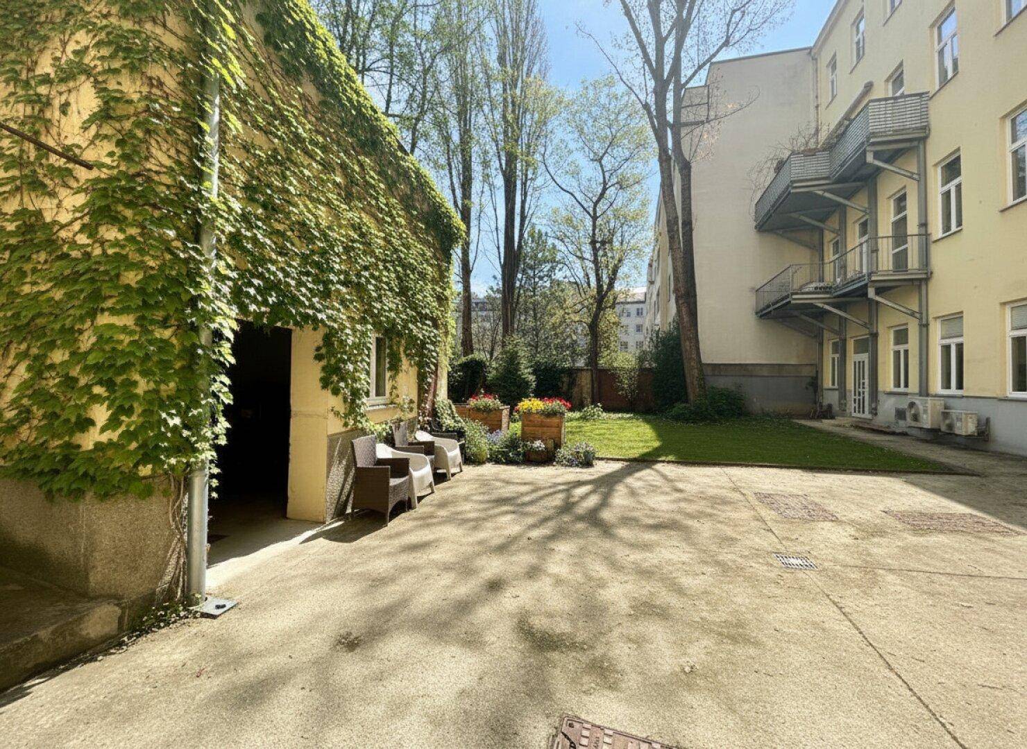 Gemeinschaftsgarten mit Sitzgelegenheiten und viel Grün, umgeben von Gebäuden.