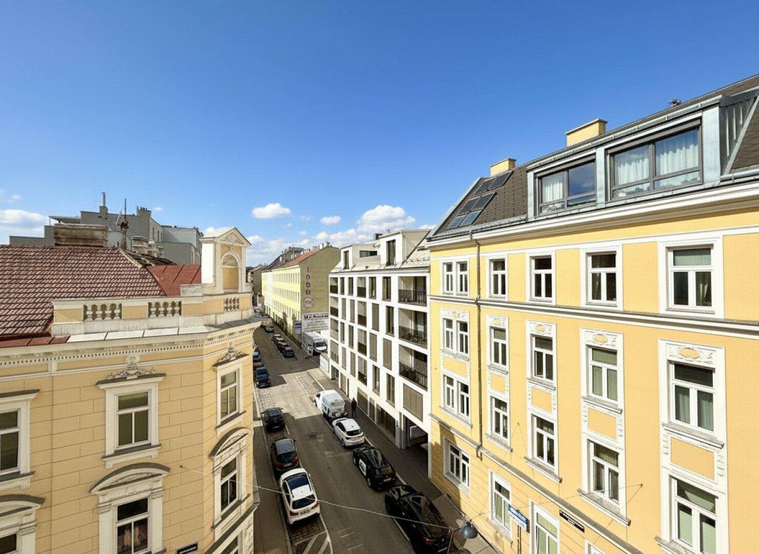 Blick von oben auf eine belebte Stadtstraße mit parkenden Autos und umliegenden Gebäuden.