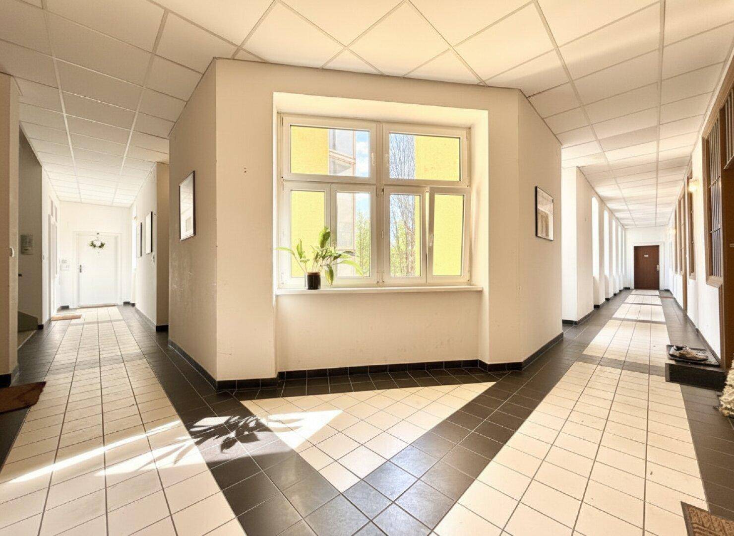 Heller Gemeinschaftsflur mit Fliesenboden und einem großen Fenster, das viel Licht hereinlässt.