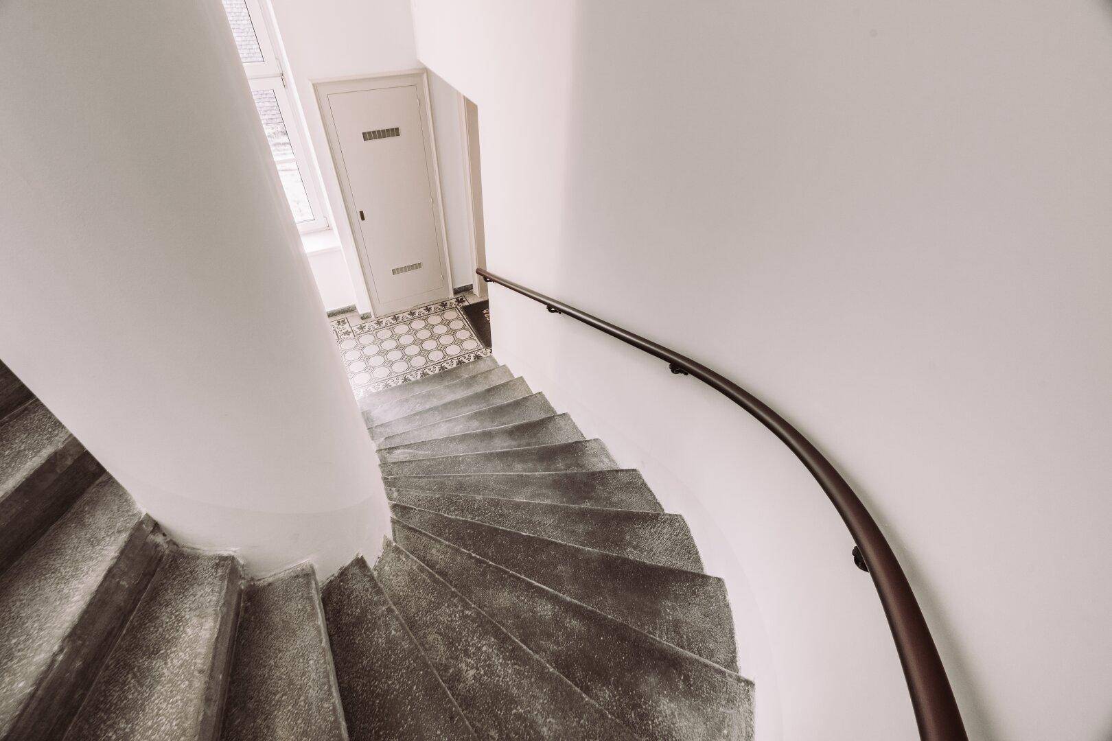 Elegantes Treppenhaus mit geschwungener Steintreppe und schmiedeeisernem Geländer in einem Altbau.