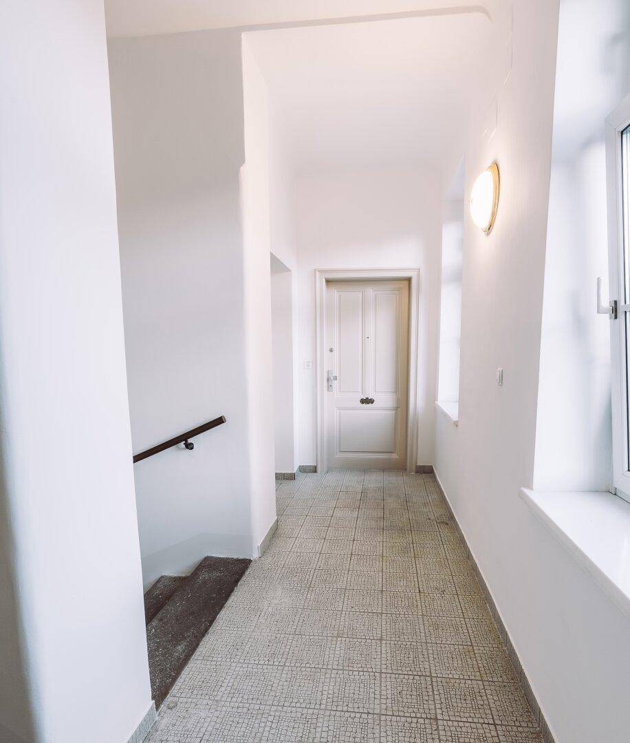 Langer, heller Flur mit Fliesenboden, weißen Wänden und einem Fenster für natürliches Licht.