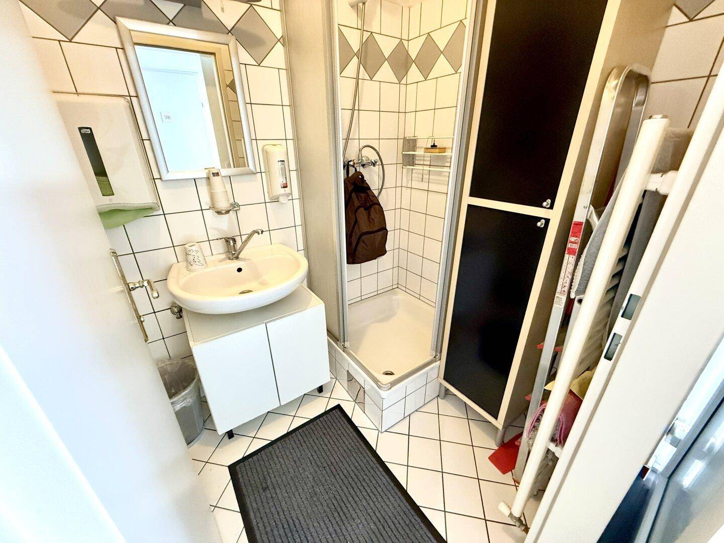 Kleines Badezimmer mit Dusche, Waschbecken und weißen Fliesen, praktisch und sauber.