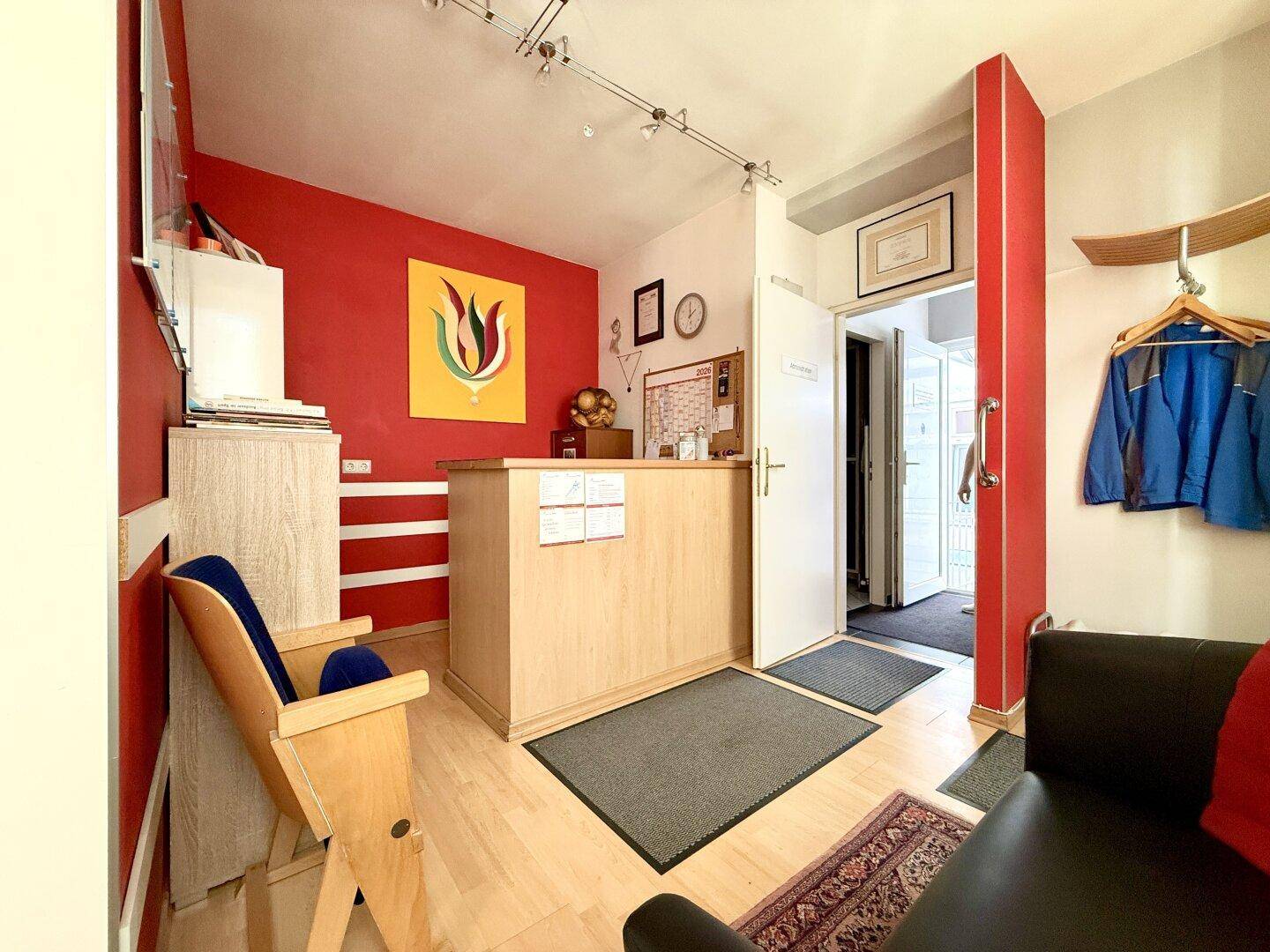 Empfangsbereich mit Theke, roter Akzentwand und Garderobe, einladend gestaltet.