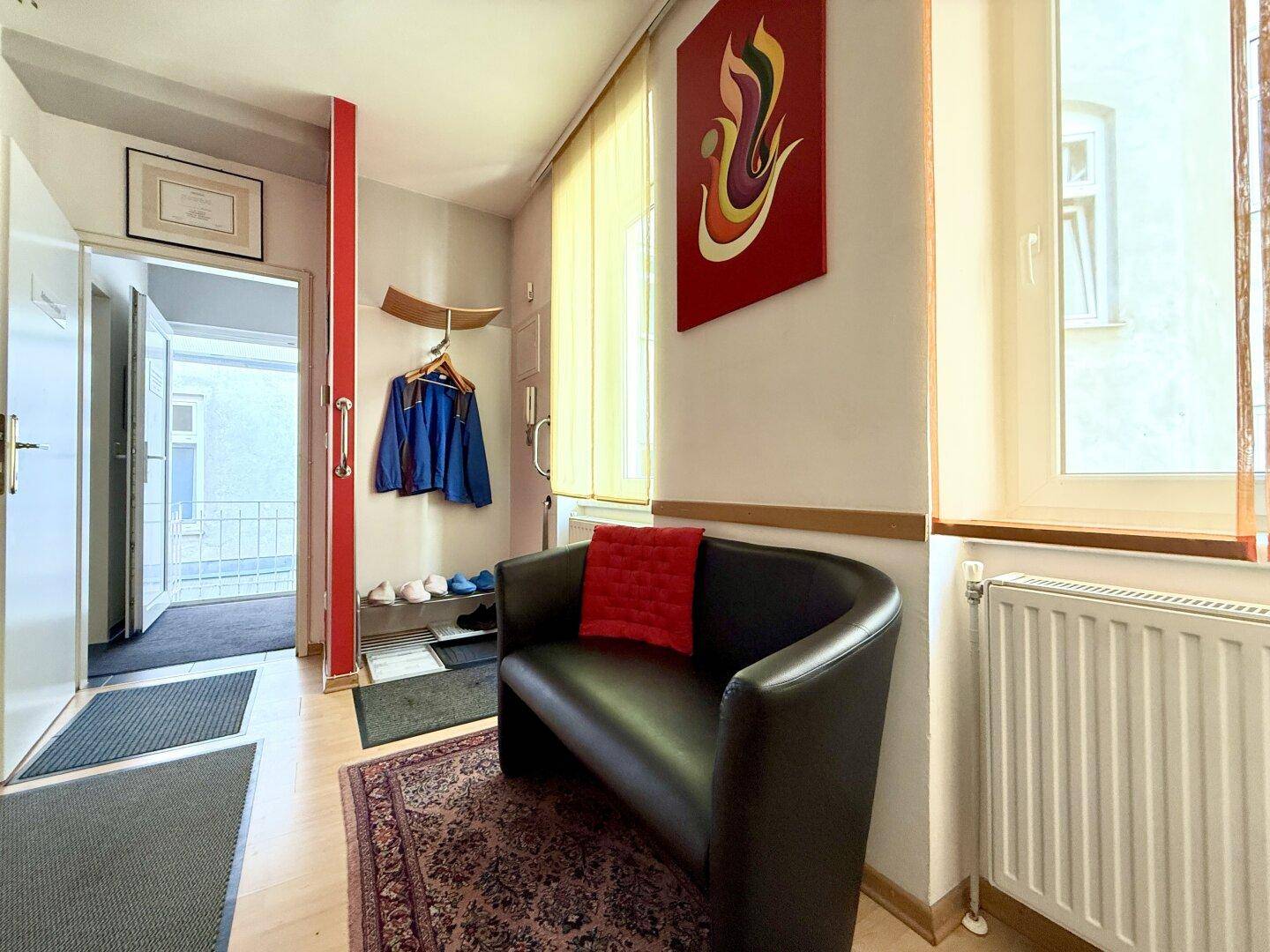 Empfangsbereich mit Sitzgelegenheit, Garderobe und Fenster, das Tageslicht hereinlässt.