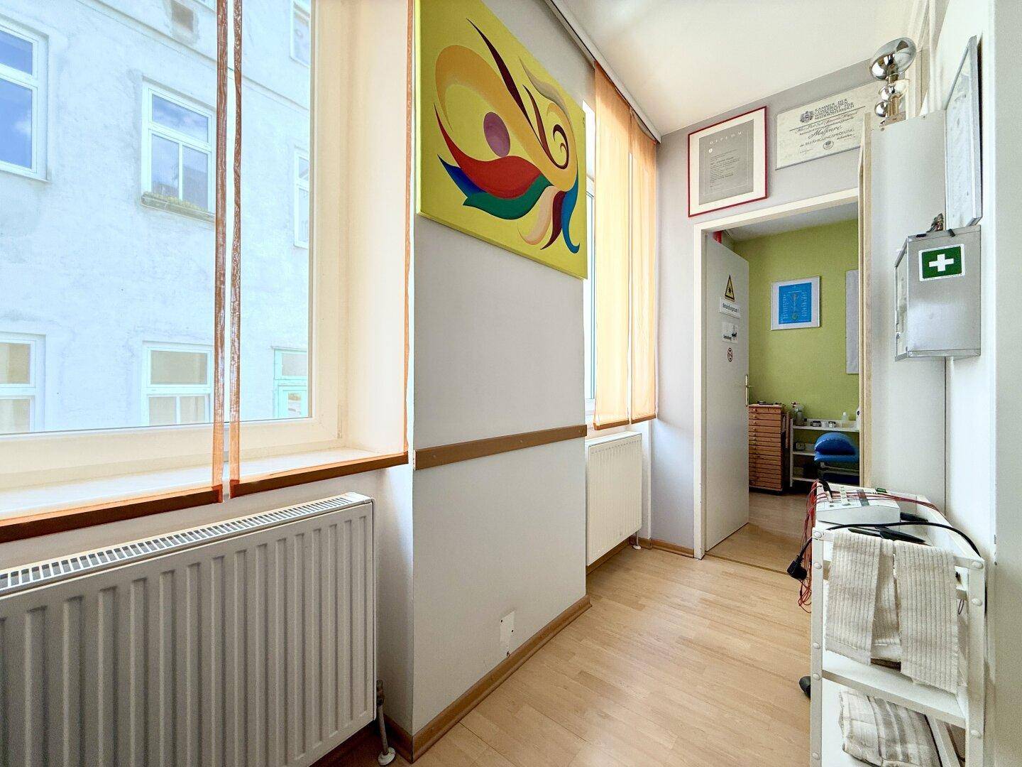 Heller Flur mit Holzboden und Fenstern, die einen Blick auf die umliegenden Gebäude bieten.