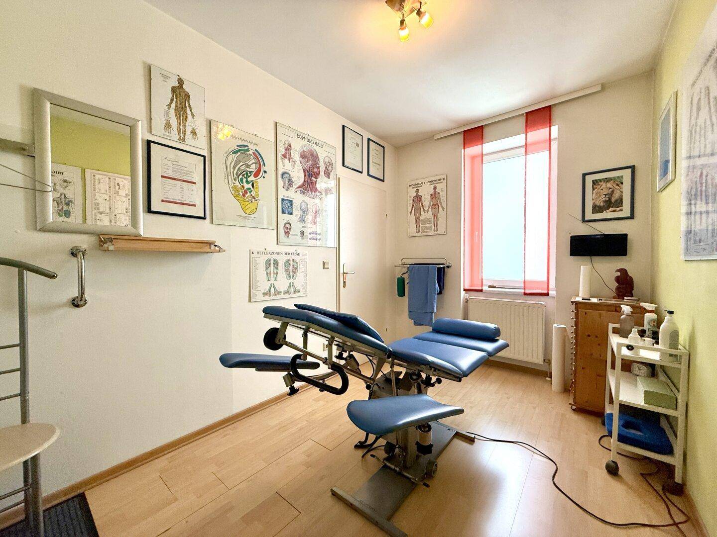Behandlungsraum mit medizinischer Liege, Holzboden und Fenster, ausgestattet für therapeutische Zwecke.